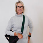 Woman wearing a gray outfit with a black handbag against a plain background