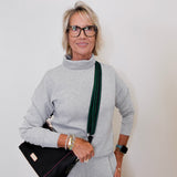 Woman wearing a gray outfit with a black handbag against a plain background