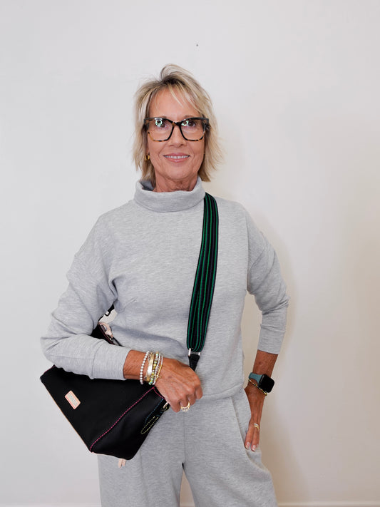 Woman wearing a gray outfit with a black handbag against a plain background