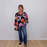 Woman wearing a floral blouse and jeans against a plain white wall.