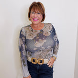 Woman wearing a floral long-sleeve top and jeans against a white wall