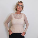 Woman wearing a beige long-sleeve top with mesh panels against a white background