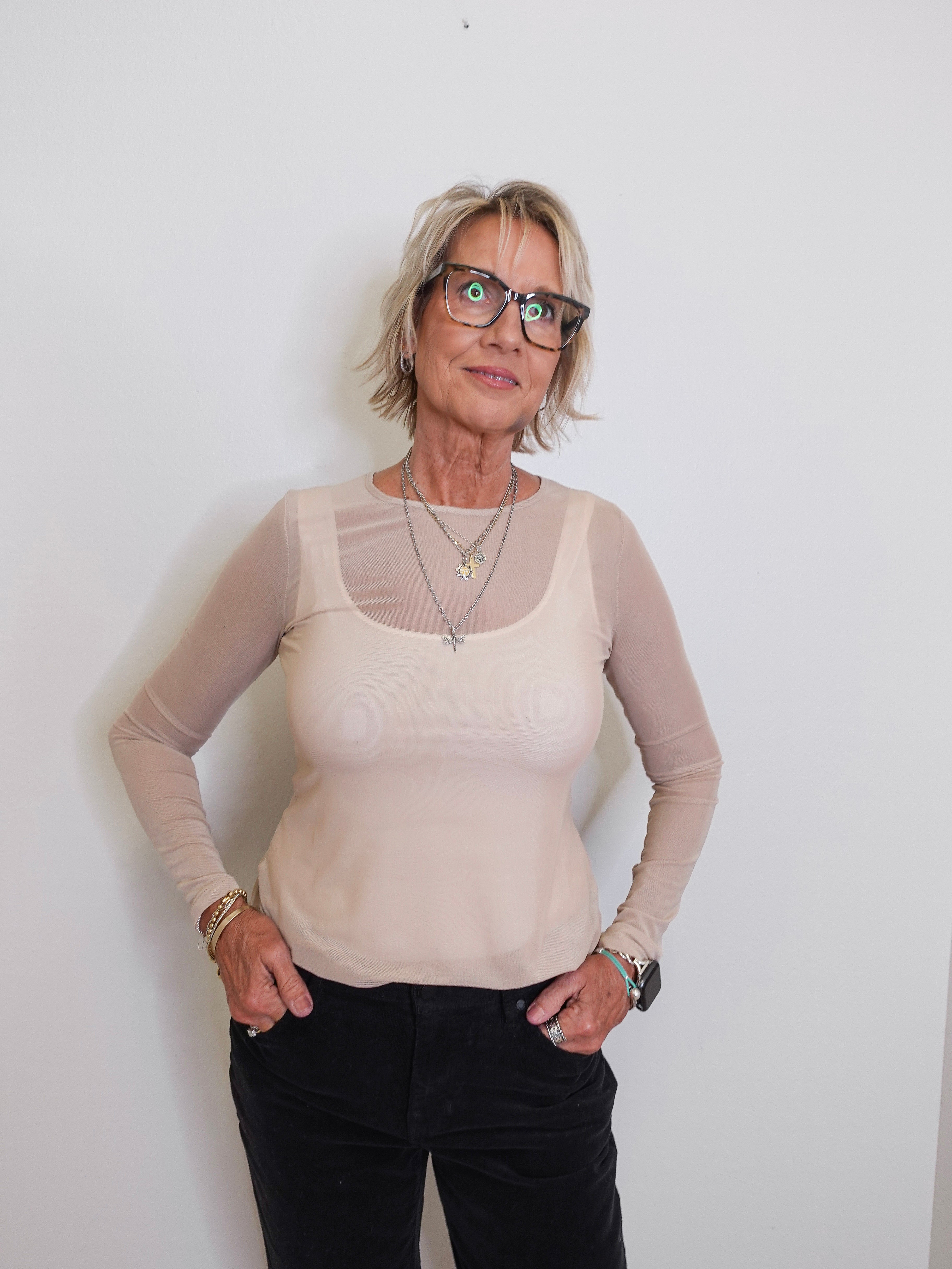 Woman wearing a beige long-sleeve top with mesh panels against a white background