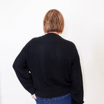 Person wearing a black sweater and blue jeans against a white background