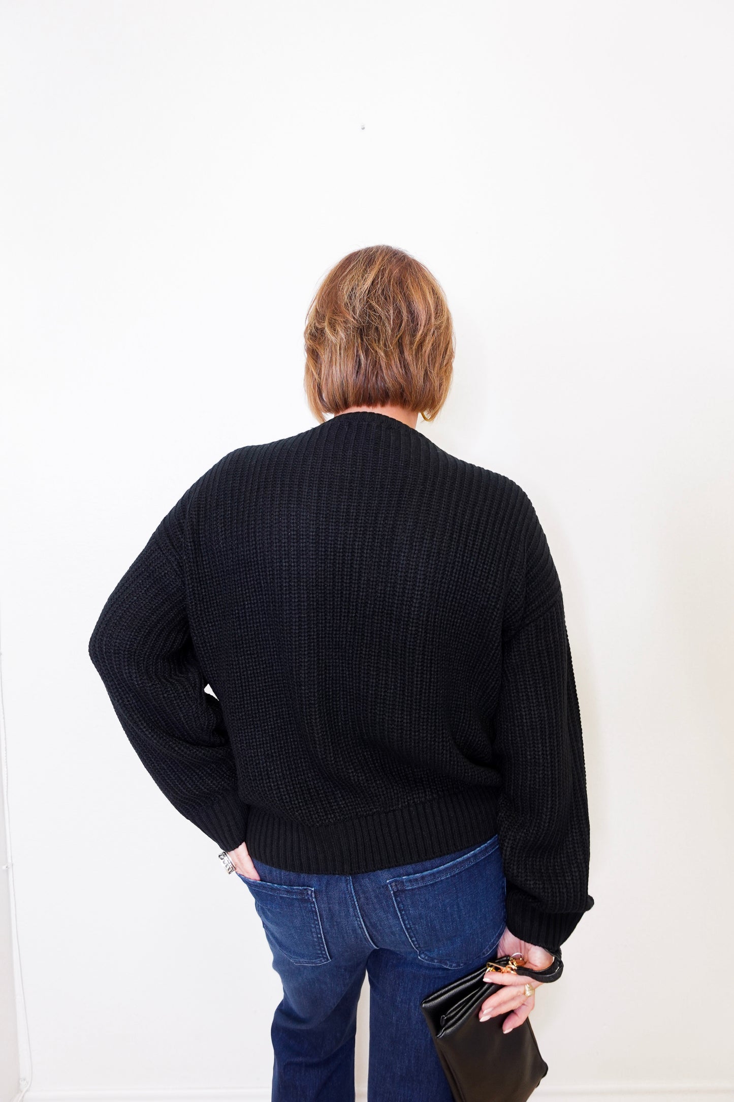 Person wearing a black sweater and blue jeans against a white background