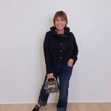 Woman wearing a black coat and jeans, holding a leopard print handbag against a white wall.