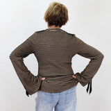 A person viewed from behind wearing a brown and beige horizontally striped long-sleeve top with flared cuffs and light blue jeans, standing against a plain white wall.
