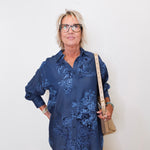 Person wearing a blue floral shirt and beige pants against a white wall