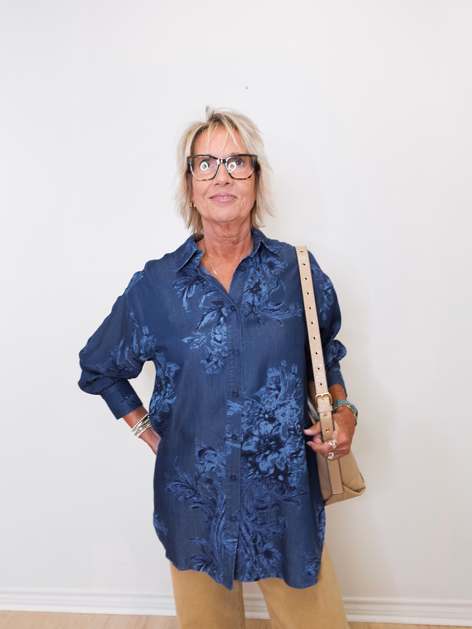 Person wearing a blue floral shirt and beige pants against a white wall