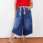 Person wearing a red top and blue denim culottes against a white background