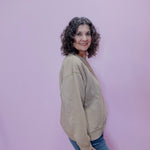 Woman wearing a beige sweater and blue jeans against a pink background