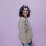 Woman wearing a beige sweater and blue jeans against a pink background