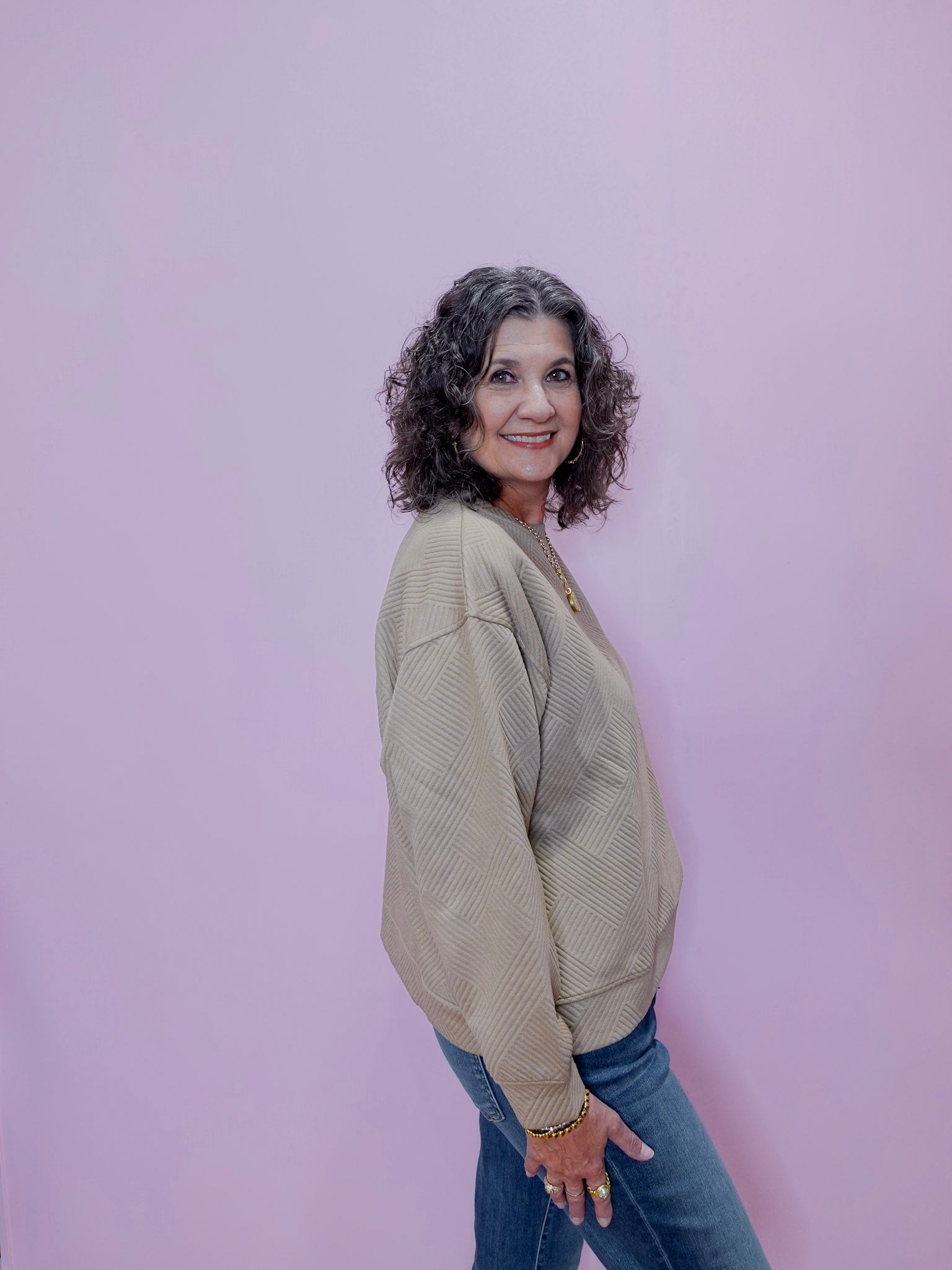 Woman wearing a beige sweater and blue jeans against a pink background