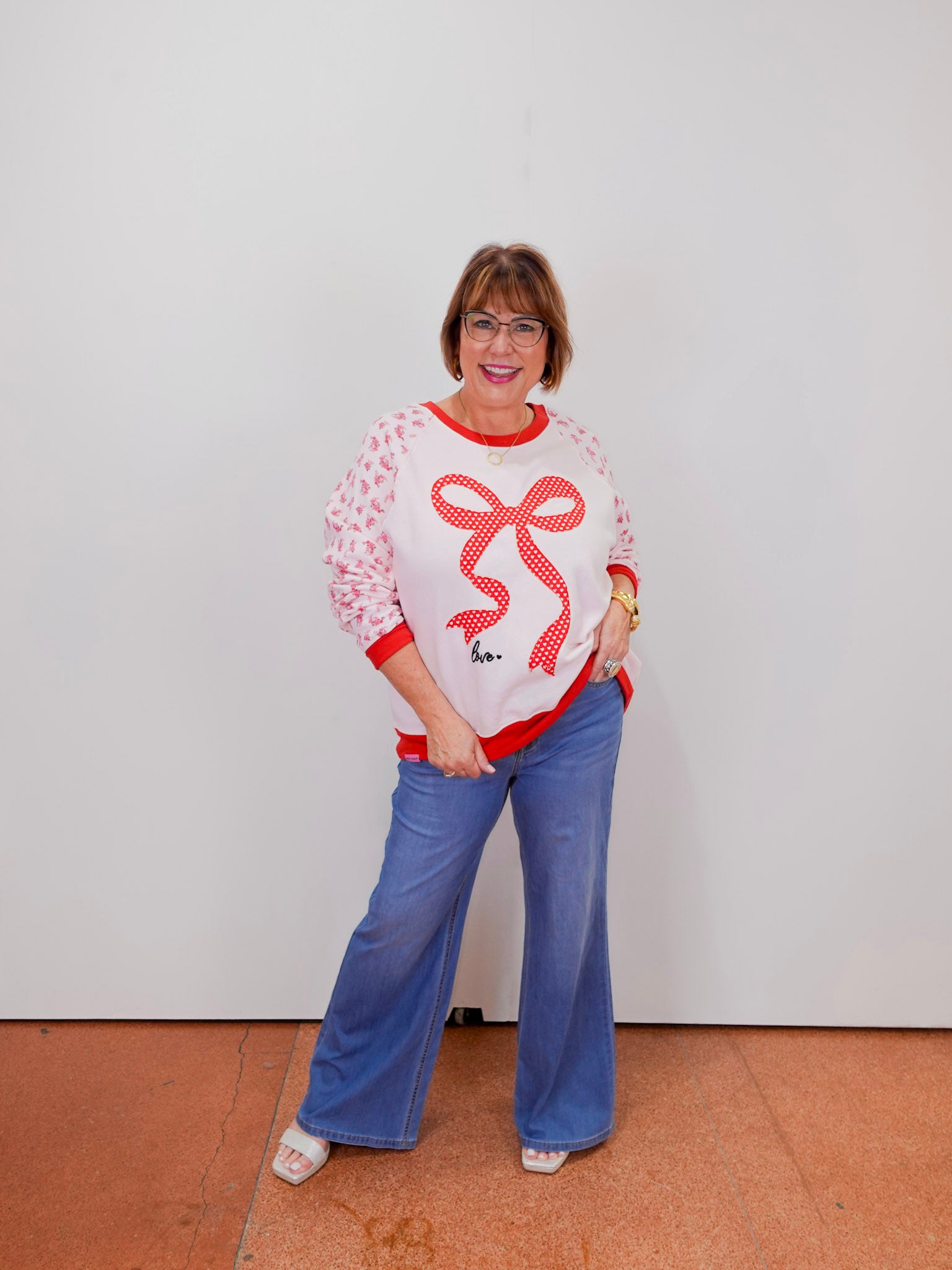 Woman wearing a white sweater with red accents and blue pants against a plain background