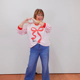 Person wearing a white sweatshirt with a red design and blue jeans against a plain background