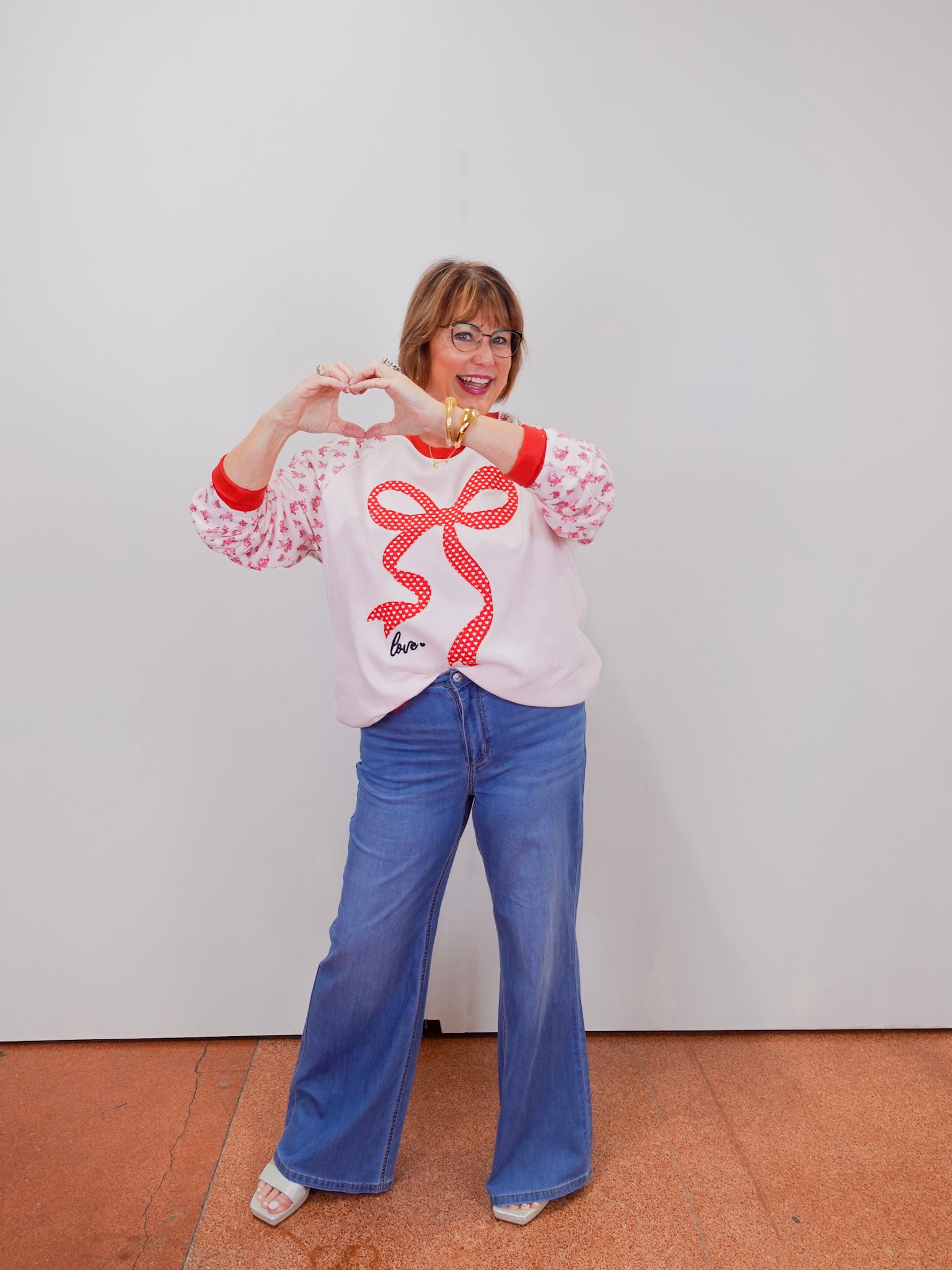 Person wearing a white sweatshirt with a red design and blue jeans against a plain background