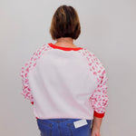 Person wearing a white sweatshirt with red accents and floral sleeves against a plain background