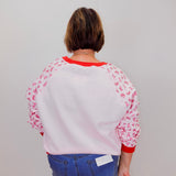 Person wearing a white sweatshirt with red accents and floral sleeves against a plain background