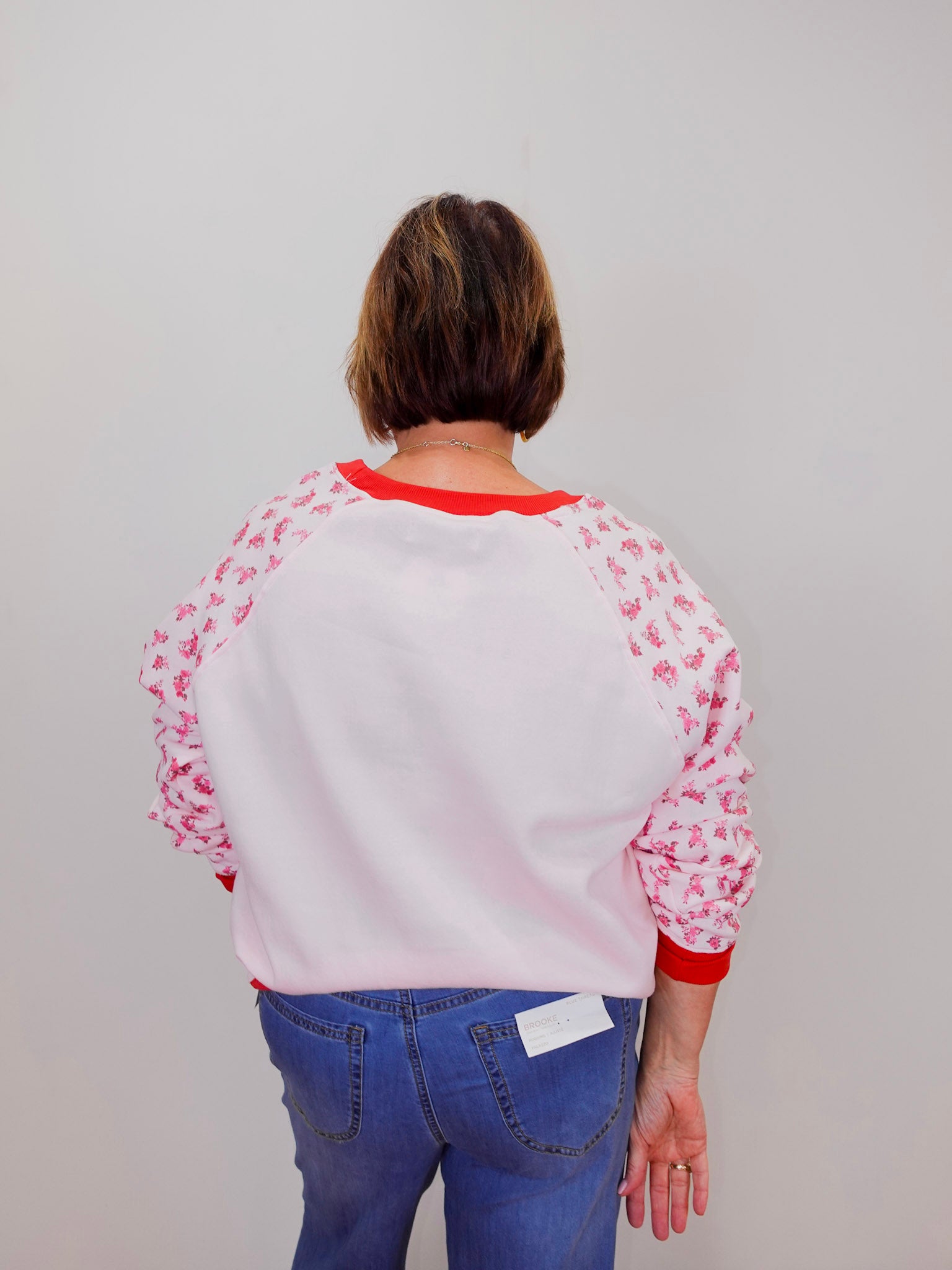 Person wearing a white sweatshirt with red accents and floral sleeves against a plain background