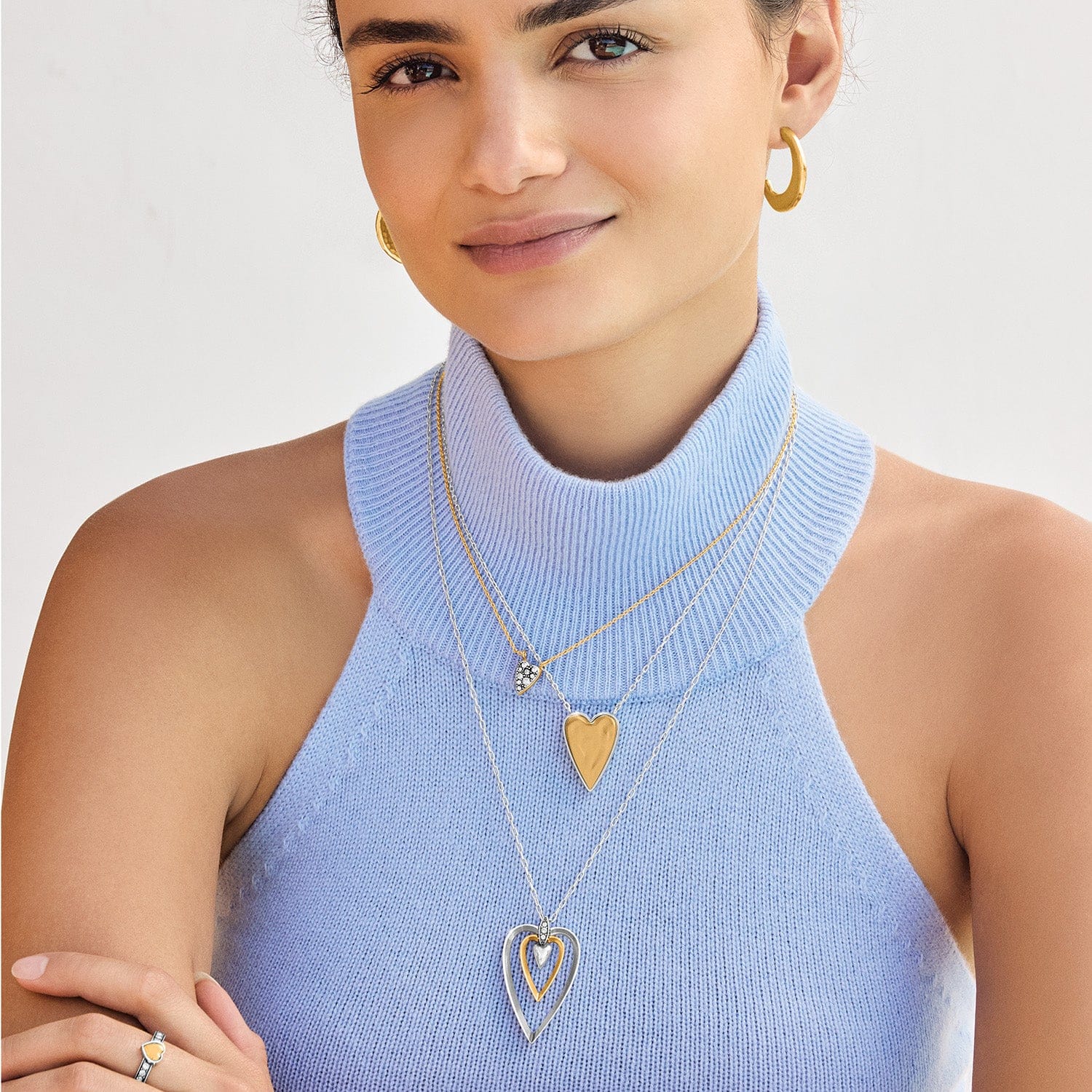 Woman wearing gold necklaces with heart pendants on a plain background
