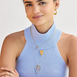 Woman wearing gold necklaces with heart pendants on a plain background