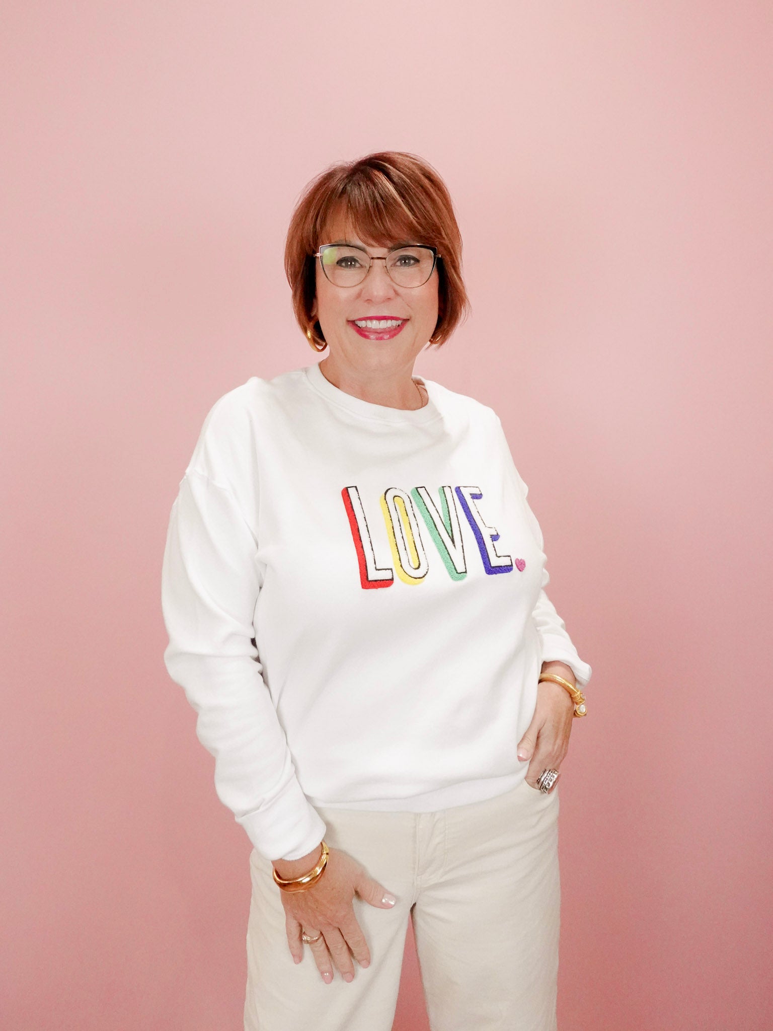 Person wearing a white sweatshirt with 'LOVE' in colorful letters against a pink background