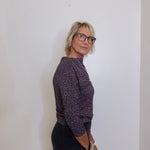 Woman wearing a patterned shirt and black pants against a plain background