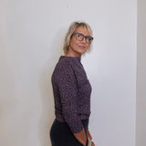 Woman wearing a patterned shirt and black pants against a plain background