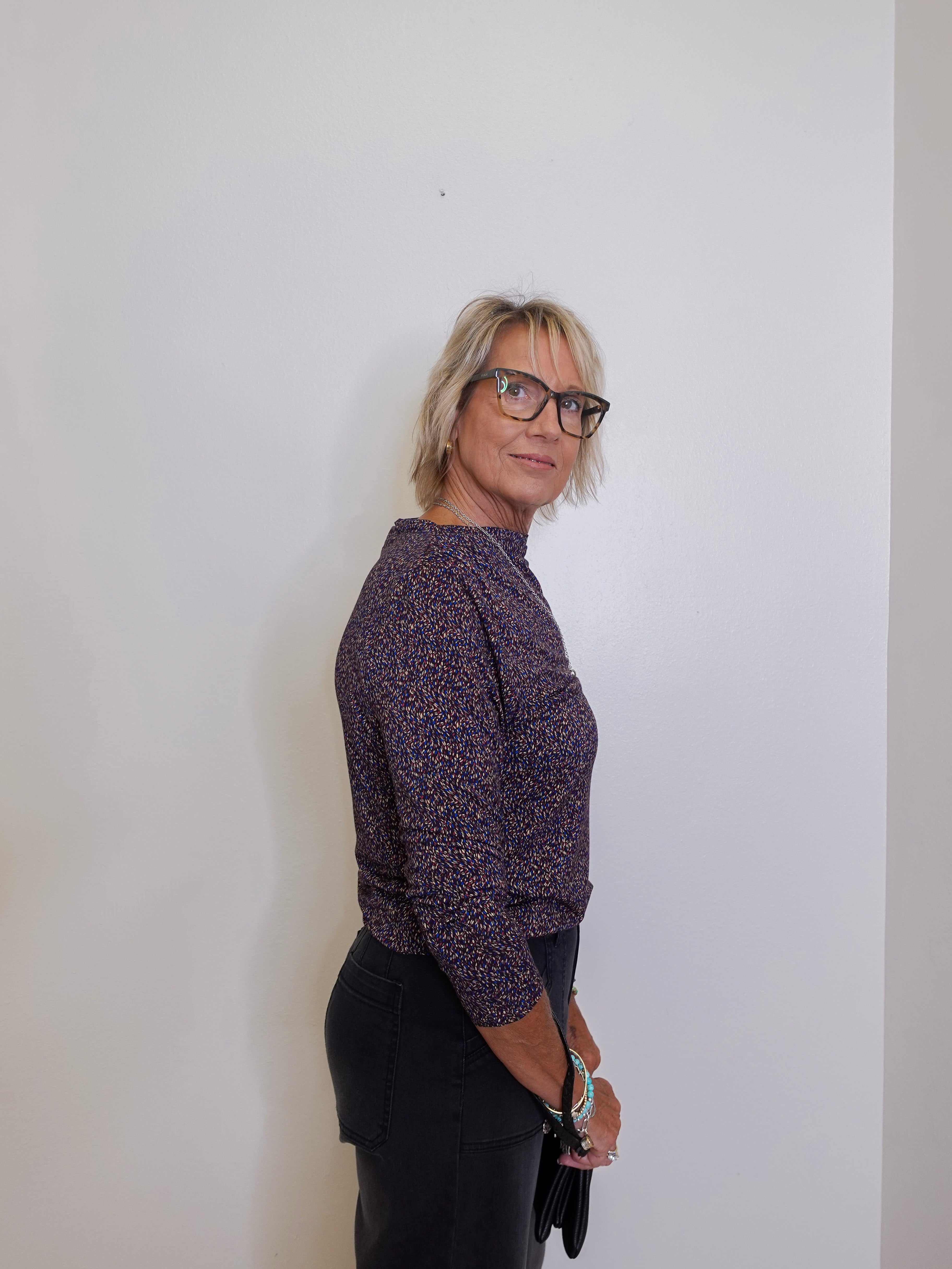 Woman wearing a patterned shirt and black pants against a plain background