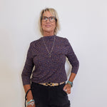 Woman wearing a patterned sweater and black pants against a white background