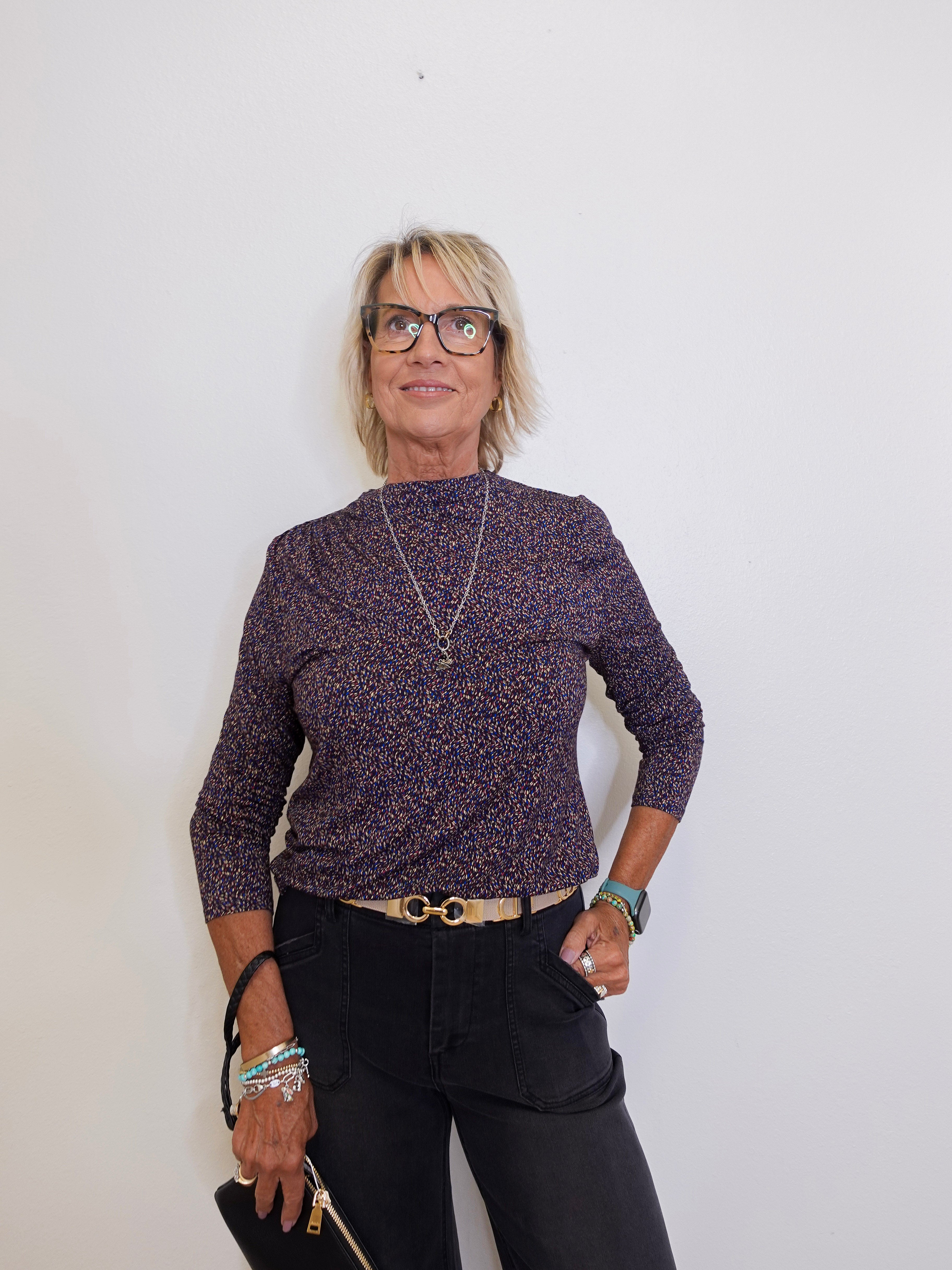 Woman wearing a patterned sweater and black pants against a white background