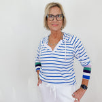 Woman wearing a striped shirt and white pants against a plain background