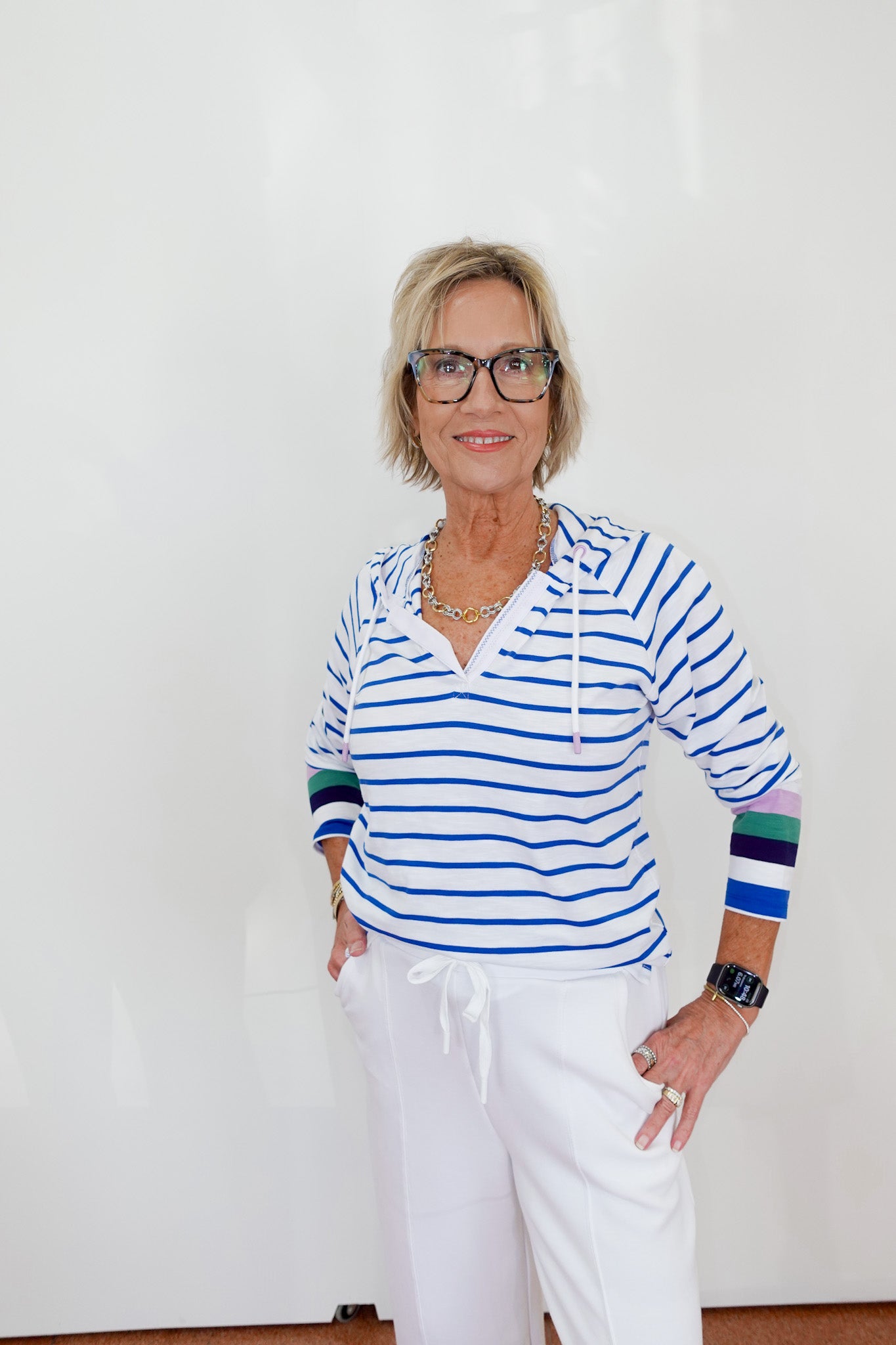 Woman wearing a striped shirt and white pants against a plain background