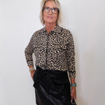 Woman wearing a leopard print shirt and black skirt against a white wall.
