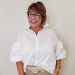Woman wearing a white shirt and beige pants against a plain background