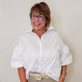 Woman wearing a white shirt and beige pants against a plain background