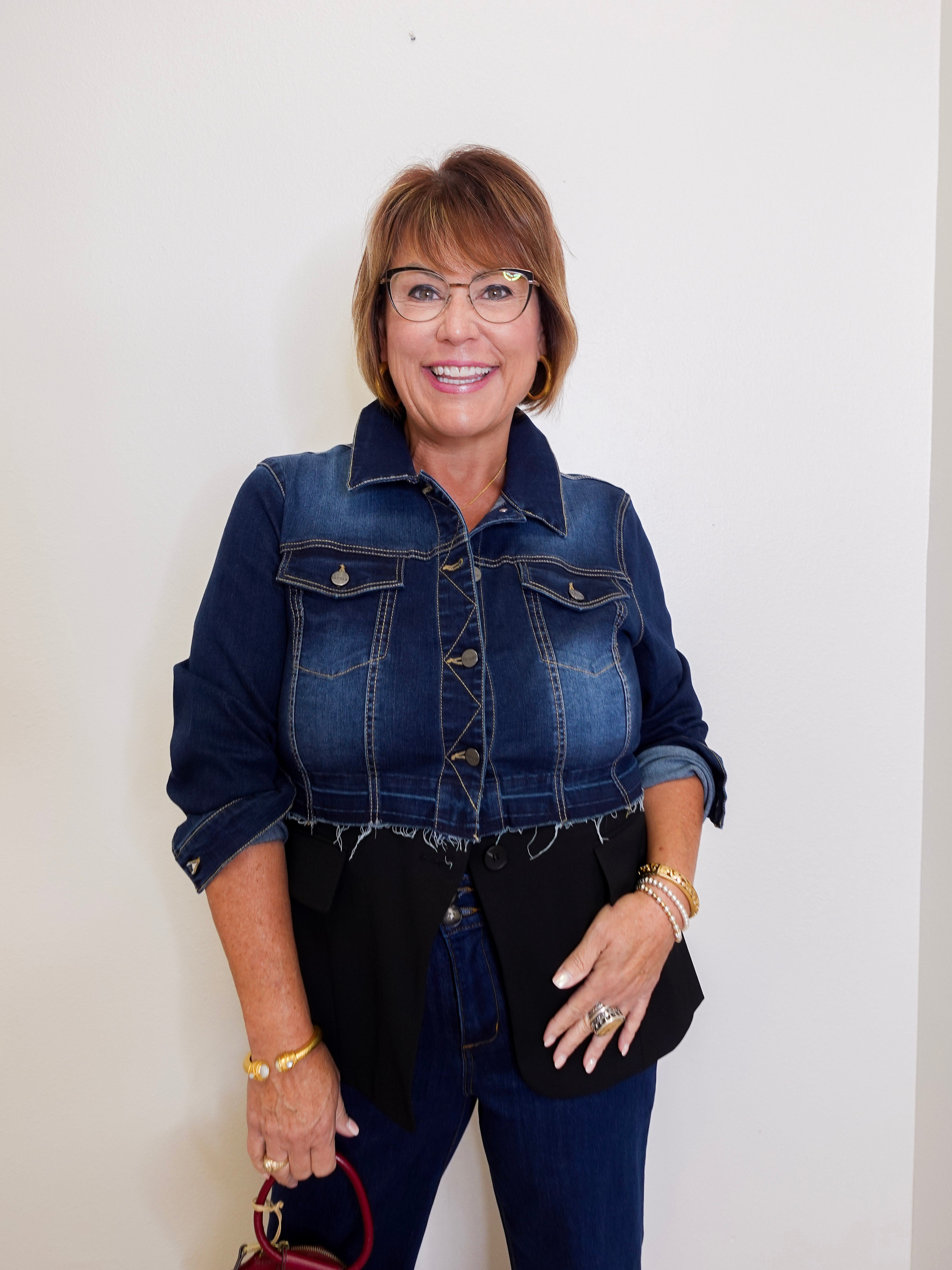 Woman wearing a denim jacket and black top against a white background