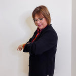 Woman wearing a black coat and glasses against a white wall