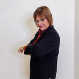 Woman wearing a black coat and glasses against a white wall