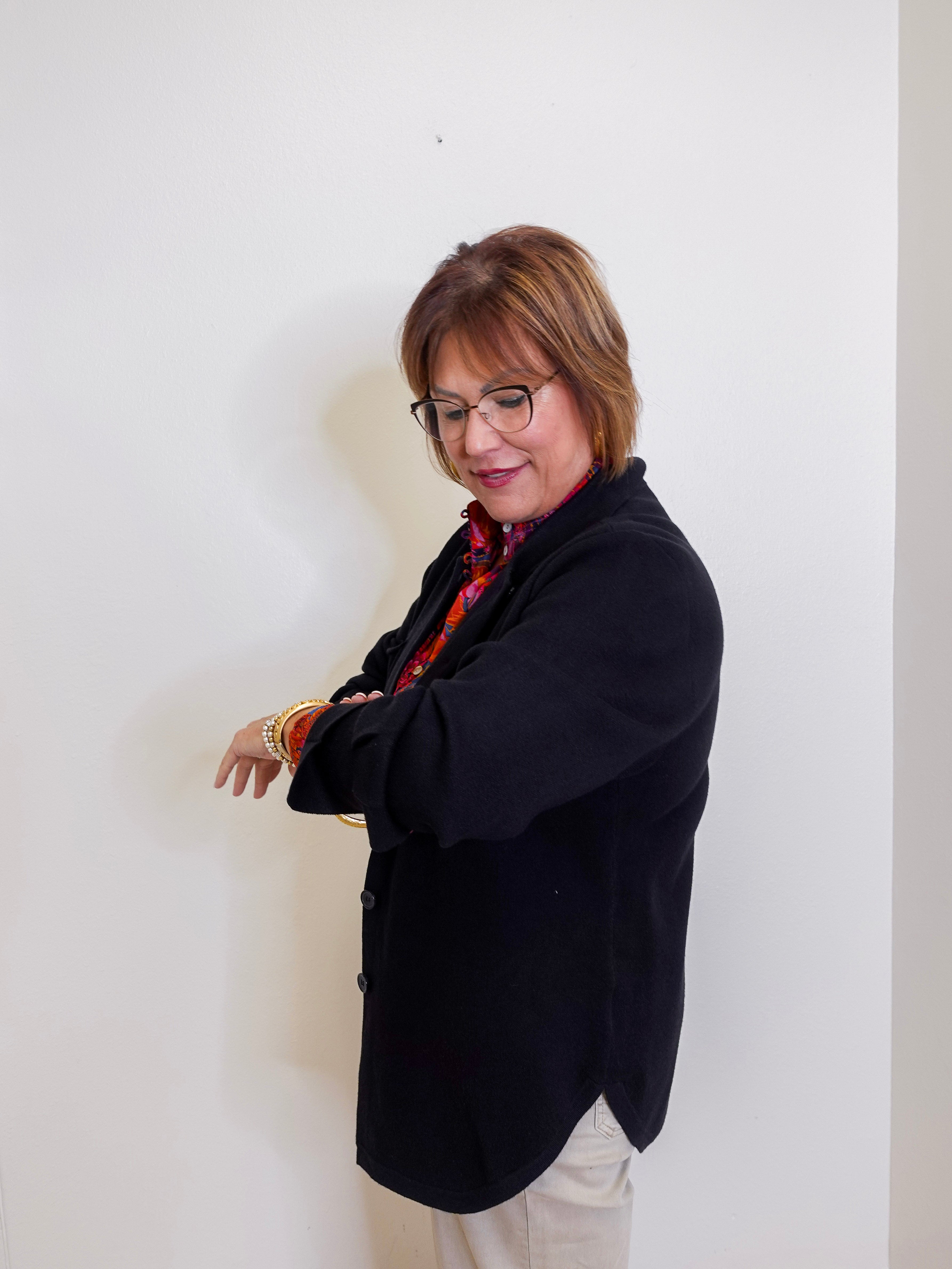 Woman wearing a black coat and glasses against a white wall