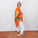 Person wearing a colorful kimono-style garment with white pants and shoes against a plain background