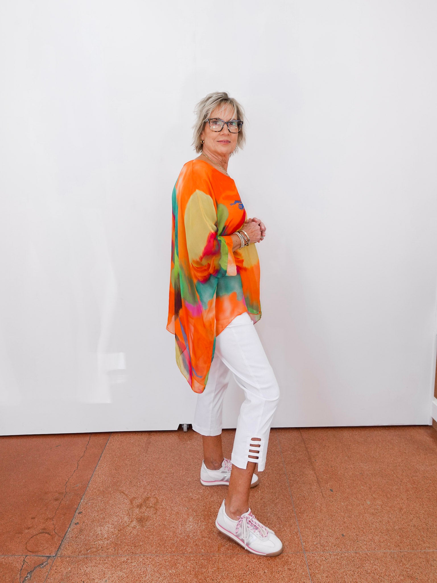 Person wearing a colorful kimono-style garment with white pants and shoes against a plain background