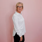 Woman wearing a white shirt and black pants against a pink wall