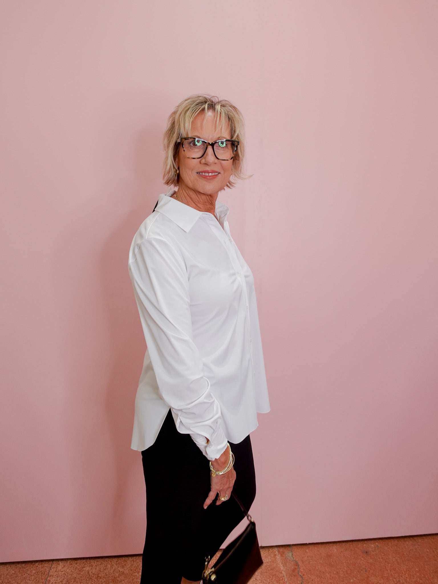 Woman wearing a white shirt and black pants against a pink wall