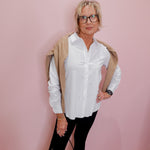 Woman wearing a white shirt, black pants, and a beige cardigan against a pink wall.