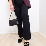 Person wearing a maroon blazer, black pants, and black shoes with gold accents, holding a black handbag.