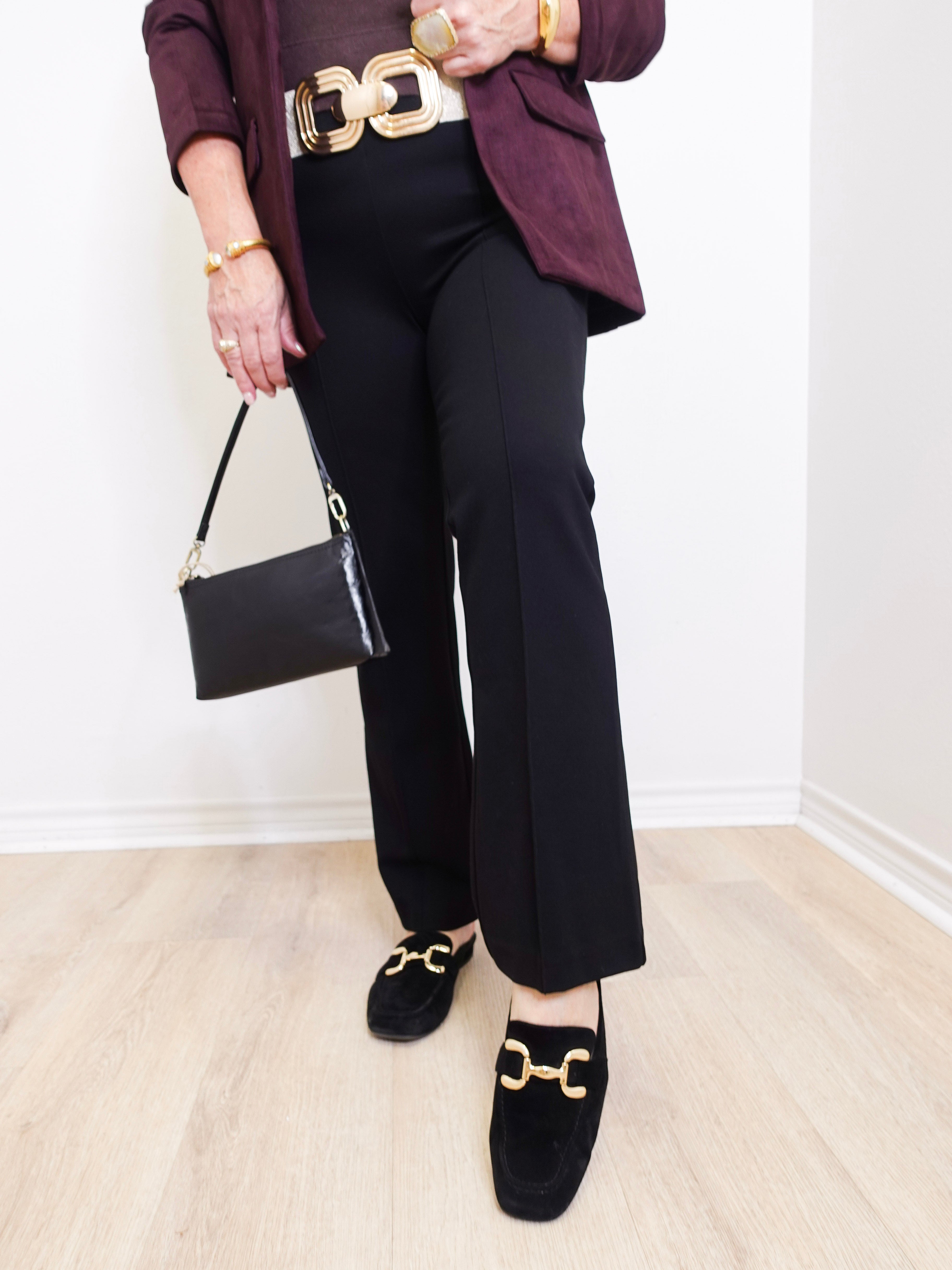 Person wearing a maroon blazer, black pants, and black shoes with gold accents, holding a black handbag.
