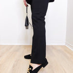 Person wearing black pants and loafers on a light wooden floor.