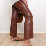 Person wearing brown leather pants and tan loafers against a white wall.