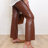 Person wearing brown leather pants and tan loafers against a white wall.